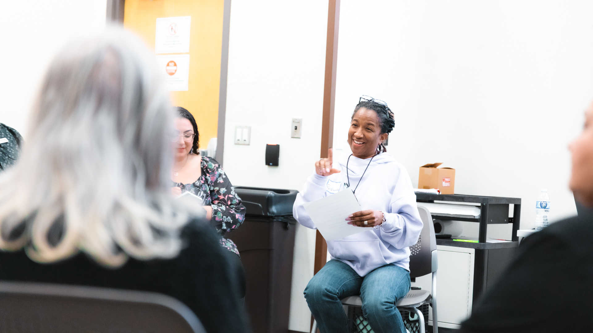 An educator smiles and gestures with her hands in a room with other educators